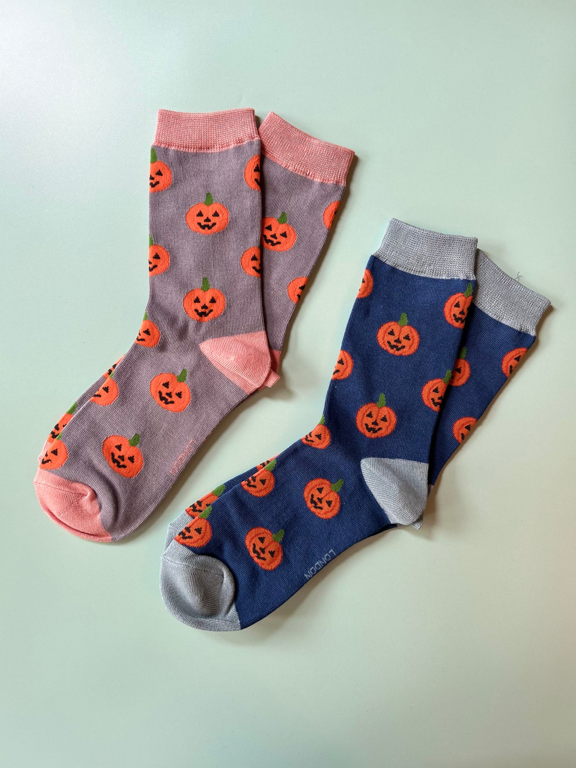 Two pairs of socks with pumpkin patterns on a light green background